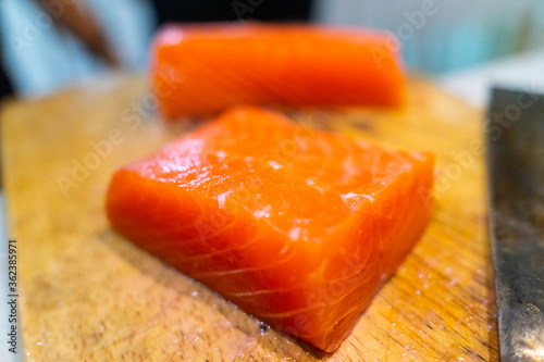 fresh raw salmon sashimi. is being cut with a knife and lying on a cutting board.