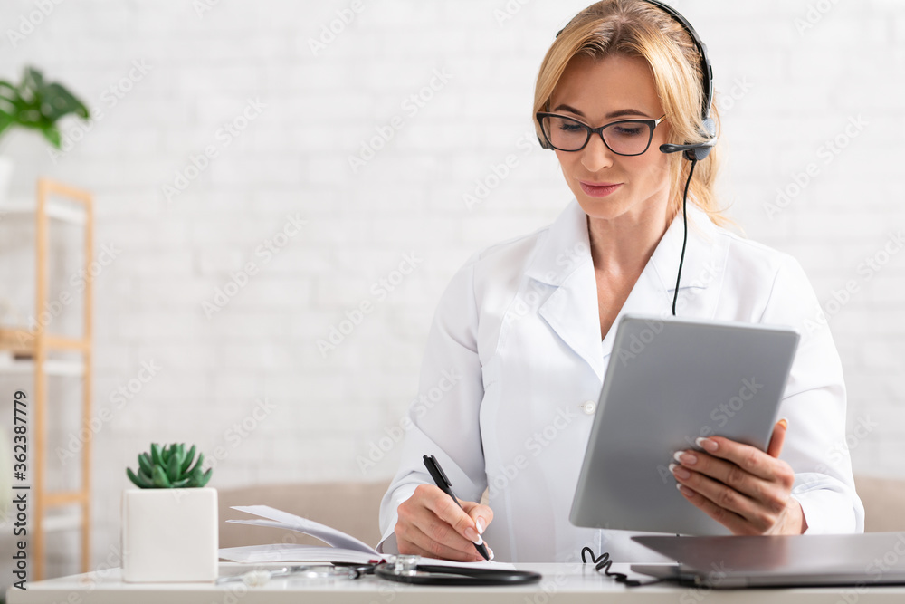 Workplace of online medical consultant. Woman with tablet in hands makes notes in notebook Workplace of online medical consultant. Woman with tablet in hands makes notes in notebook