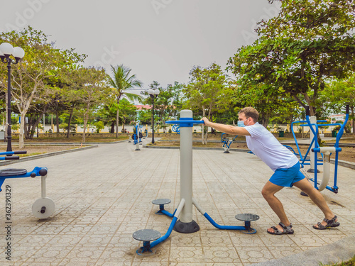Man doing physical exercises, push ups, strength exercises, leans in empty outdoor public city park metal gym wearing mask alone for Covid19 prevention. Healthy lifestyle in quarantine and coronavirus