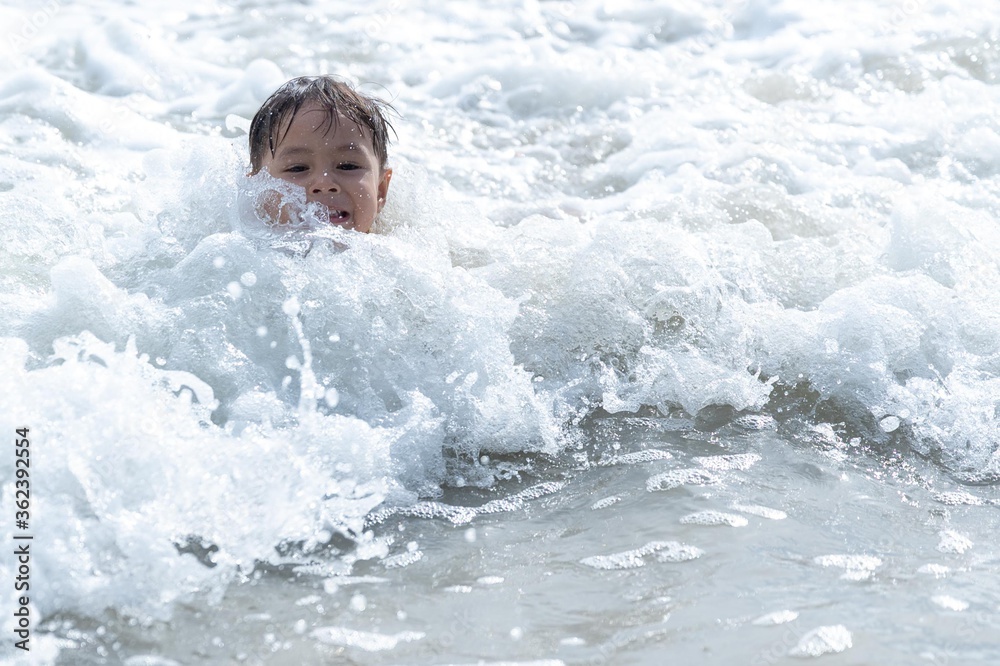 Little boy playing and splashing in sea waves