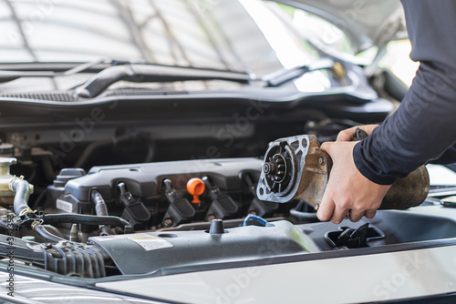 Mechanic man holding starter motor of the car on working table in repair and maintenance garage