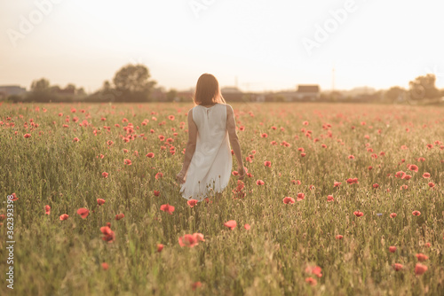 Beautiful girl stands in a poppy field backwards