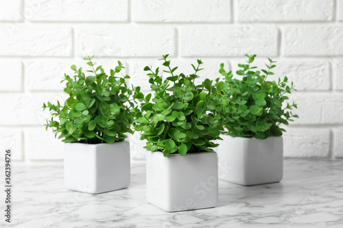 Beautiful artificial plants in flower pots on white marble table near brick wall