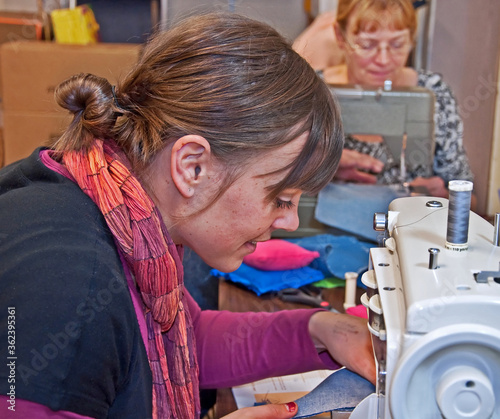 These two Caucasian women are sewing on sewing machines  one is middle aged  and the other is a young adult learning how.
