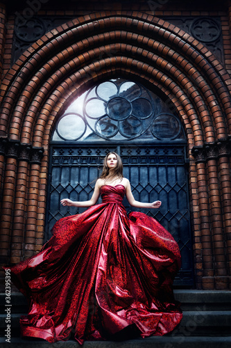 Fashion Model near Medieval Castle Gate Door, Woman Beauty Glamour Portrait in Elegant Waving Red Dress