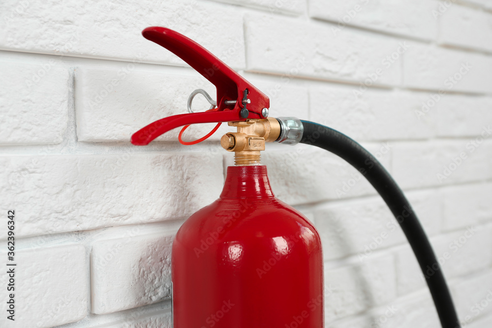 Naklejka premium Fire extinguisher near white brick wall, closeup