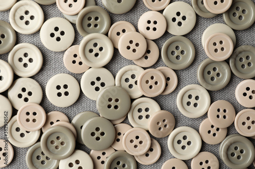 Many plastic sewing buttons on grey fabric  flat lay