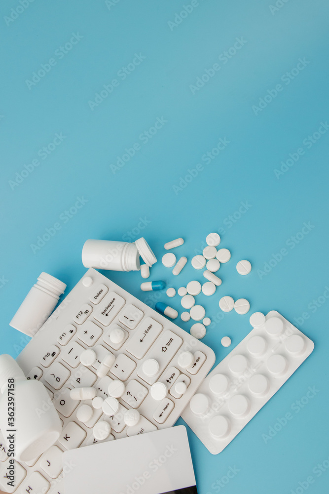Shopping cart toy with medicaments and Keyboard. Pills, blister packs, medical bottles, thermometer, protective mask on a blue background. Health care and internet shopping.