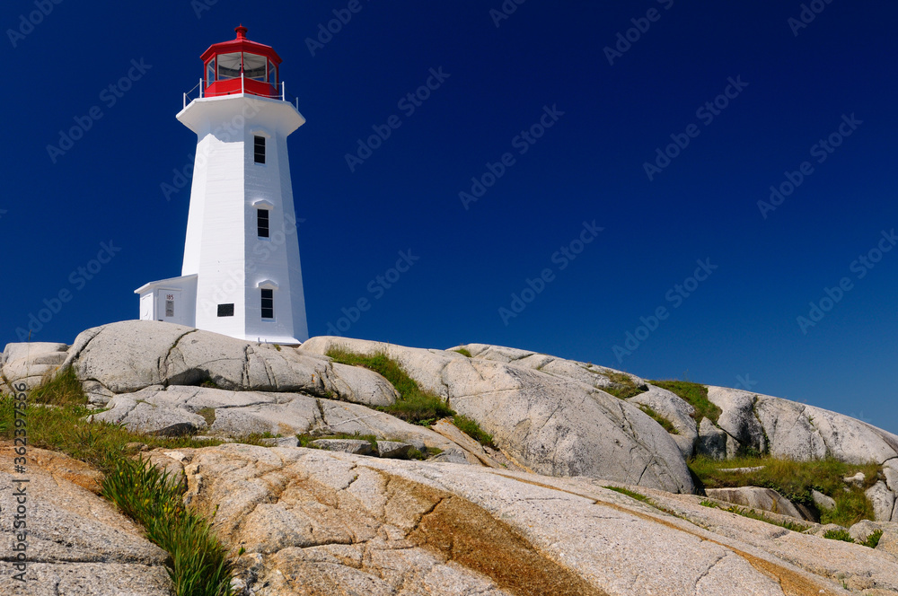 Peggys Cove lighthouse on top of smooth granite rocks against a blue sky Nova Scotia
