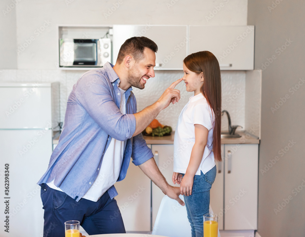 Father Touching Daughter's Nose Standing In Kitchen At Home