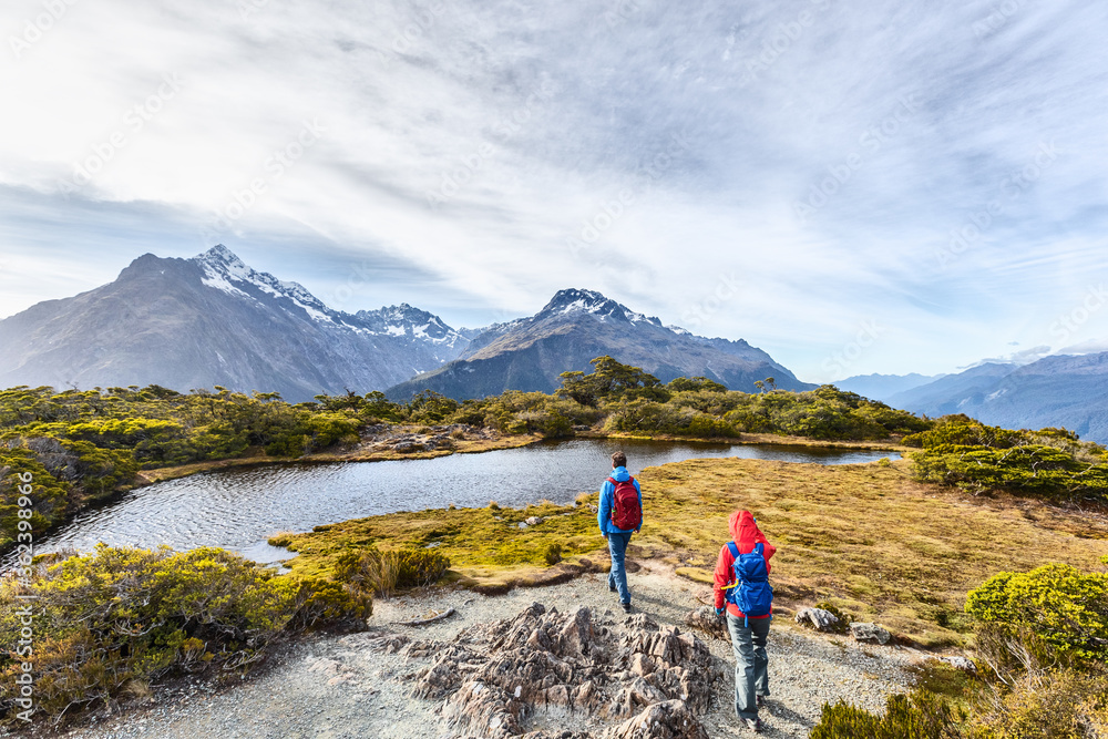 Hiking couple walking on adventure hike at Routeburn Track during sunny day. Hikers carrying backpacks tramping on Key Summit Track. People on vacation at Fiordland National Park, New Zealand.