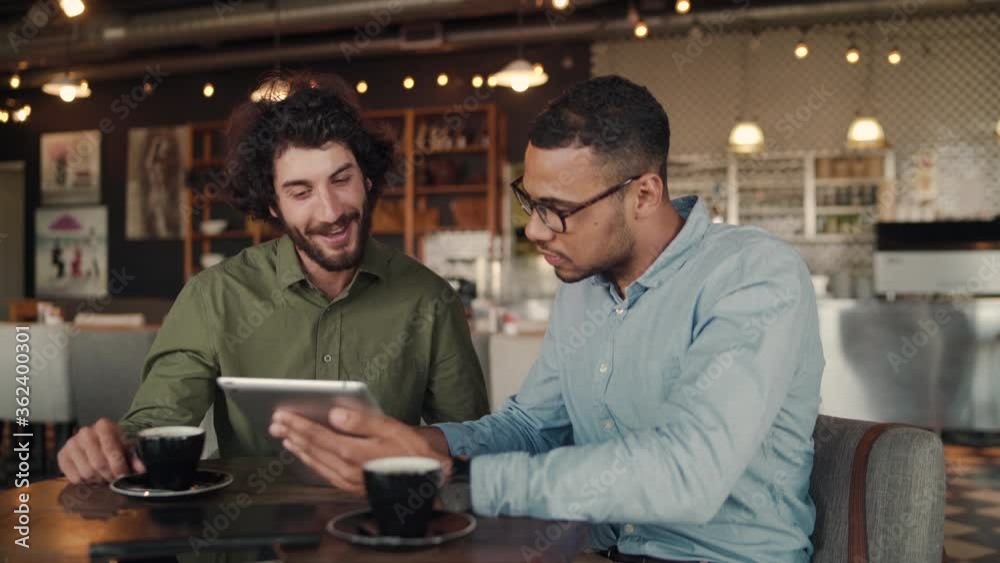 African sales man showing company services to customer sitting in modern cafe using digital tablet
