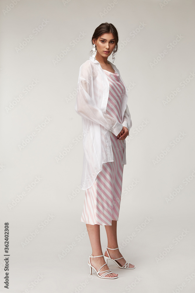 Sexy fashion model beautiful woman pretty face makeup, tanned skin wear summer collection clothes style for romantic date walk trendy light silk in white pink stripes long dress white shirt earrings. Sexy fashion model beautiful woman pretty face makeup, tanned skin wear summer collection clothes style for romantic date walk trendy light silk in white pink stripes long dress white shirt earrings.