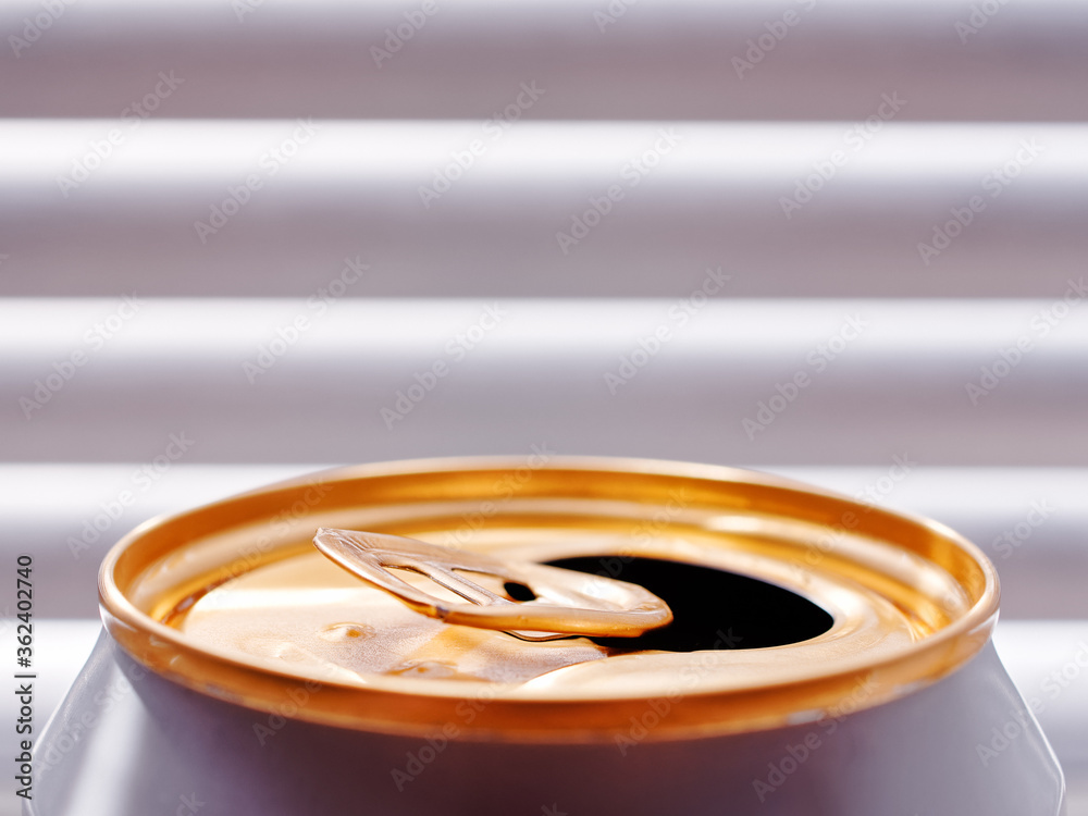 Close view of an open can with beer, soda or other drink. Golden can aluminum top. Blinds are on the background. The concept of cooling in hot weather. Close view of an open can with beer, soda or other drink. Golden can aluminum top. Blinds are on the background. The concept of cooling in hot weather.