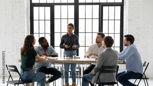 Indian business trainer teach multi-ethnic members during training seminar activity, coach stand in front of staff speaking about corporate goals, methods to succeed them. Negotiations meeting concept