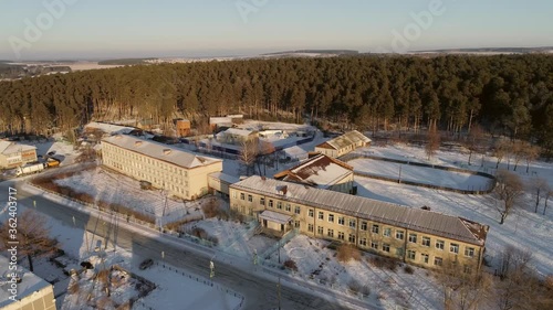 01. Aerial view of School in the village. Winter, sunny. Behind the school hockey court and forest. It's snowing outside. Russia, Sverdlovsk region, Sysert district, Oktyabrskiy

 photo