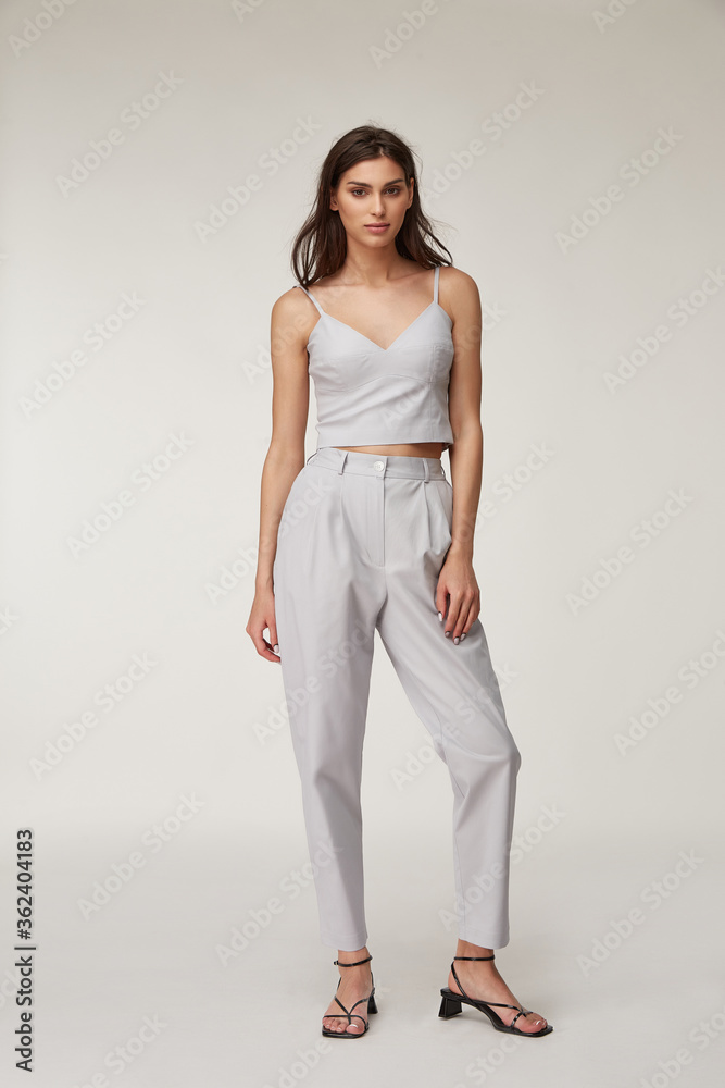 Fashion pretty woman beautiful makeup perfect body shape tanned skin wear clothes summer collection organic textile cotton light gray suit crop top and trousers stylish sandals shoes.