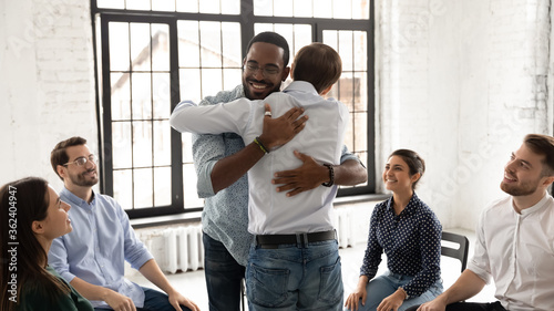 African and Caucasian millennial men embracing during group counselling therapy session. Multi ethnic people gather together provide each other psychological help, overcome problems addiction concept