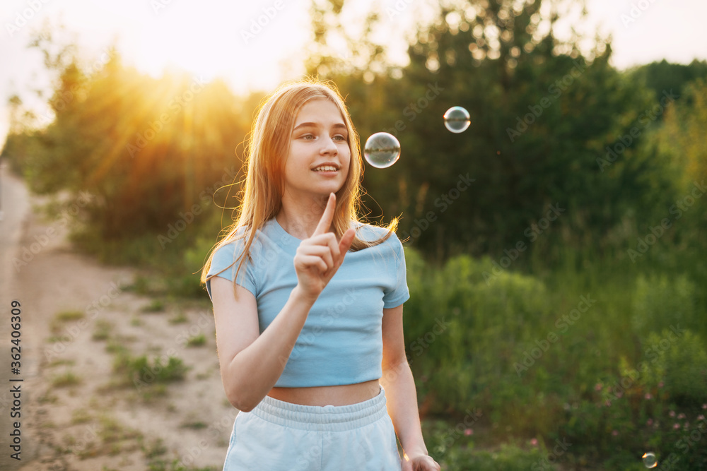 Cute girl with a beautiful smile catches soap bubbles on the background of a beautiful sunset.