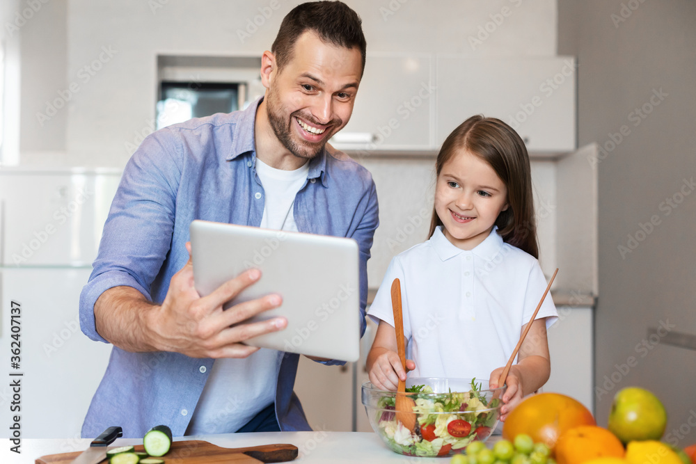 Father And Daughter Using Tablet Cooking In Kitchen At Home Father And Daughter Using Tablet Cooking In Kitchen At Home