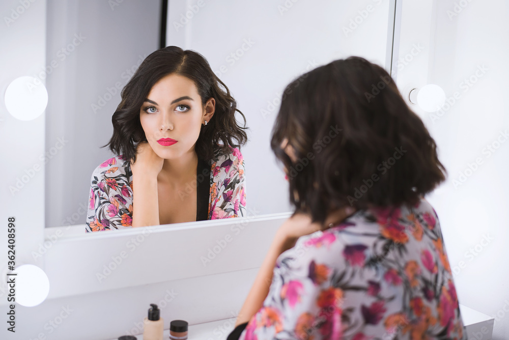Young attractive brunette model sits in front of mirror in a bathrobe ...