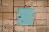Old metal small door painted with blue paint against the background of an old white tiles