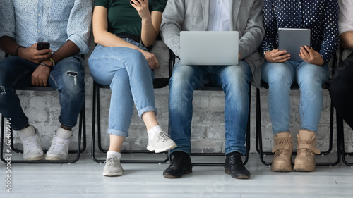 Office floor and feet view, group of diverse unemployed people sit in row in queue on chairs wait for job interview. Students ignoring each other using gadgets overuse phubbing, hr recruitment concept © fizkes