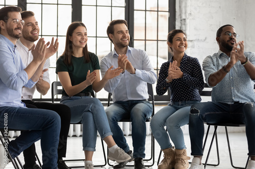 Group of cheerful employees sitting on chairs in boardroom clap hands encourage business coach start workshop. Six participants express gratitude applauding to trainer after seminar activity concept