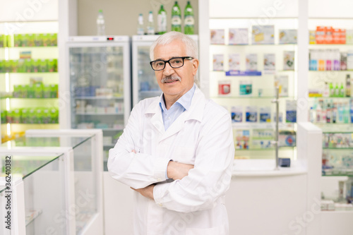 Aged successful owner of large contemporary drugstore crossing his arms by chest