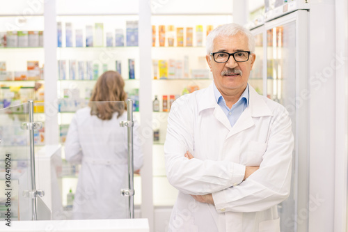 Contemporary senior expert in pharmacy and medicine standing against display
