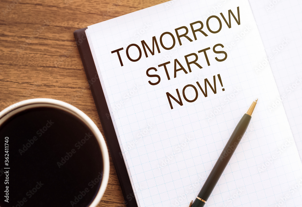 Tomorrow starts now written in a notebook with coffee and pen. Motivation concept Tomorrow starts now written in a notebook with coffee and pen. Motivation concept