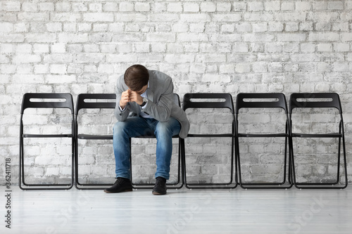 Desperate sad jobless man put head on hands sitting on chair hunched after unsuccessful failed job interview meeting. Fired employee feels stressed after dismissal, boss and company bankruptcy concept photo