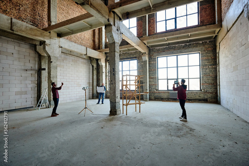 Two young contractors photographing unfinished structure inside building
