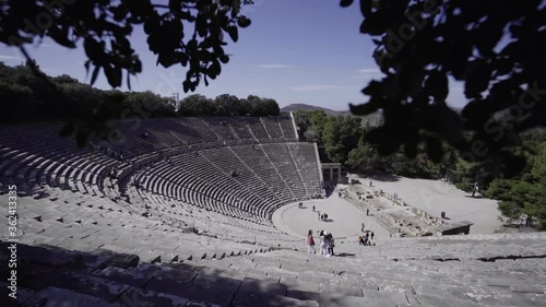 Tourists Visiting The Famous Ancient Theatre Of Epidaurus On The West Side Of Cynortion Mountain On A Sunny Day In Greece. - pan down photo