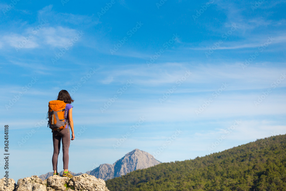 A woman with a backpack stands on top of a mountain and admires the beauty of a mountain valley. A woman with a backpack stands on top of a mountain and admires the beauty of a mountain valley.