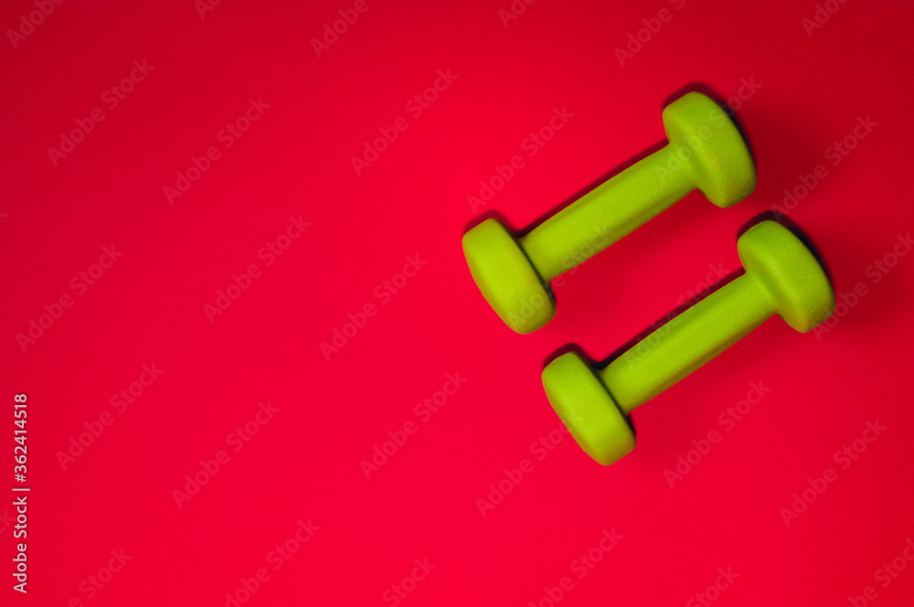 Green dumbbells isolated on a red background. Flatlay concept of fitness, gym and healthy lifestyle. The view from the top and space for copy Green dumbbells isolated on a red background. Flatlay concept of fitness, gym and healthy lifestyle. The view from the top and space for copy