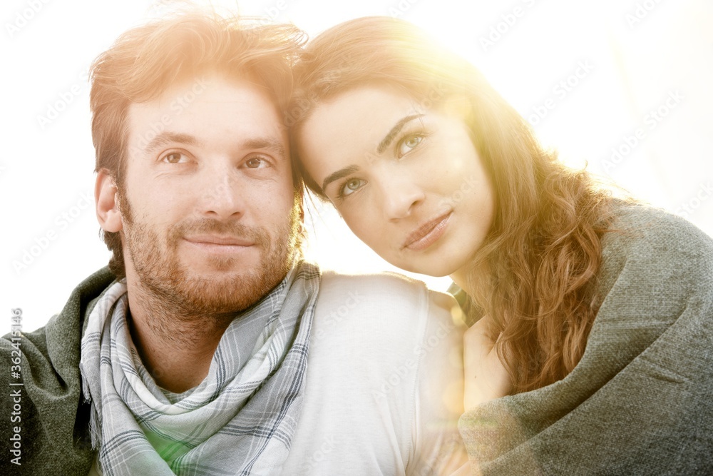 Portrait of young love couple sitting outdoor in sun light, sharing a blanket, smiling. Summer and lens flare effect. Portrait of young love couple sitting outdoor in sun light, sharing a blanket, smiling. Summer and lens flare effect.