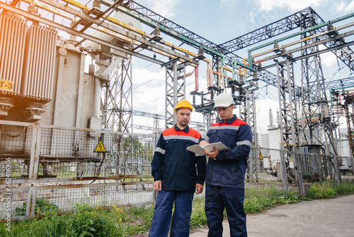 Two specialist electrical substation engineers inspect modern high-voltage equipment in the evening. Energy. Industry