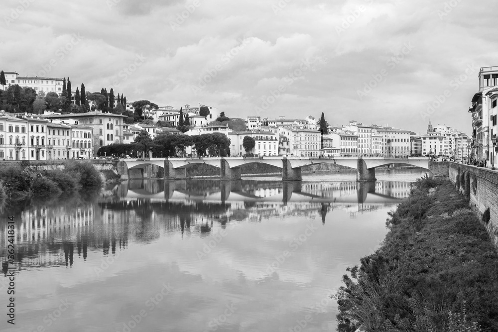 Florence or Firenze, Ponte delle Grazie bridge across the Arno river, reflections on the water, Tuscany, Italy. 
Monochrome image, black and white.