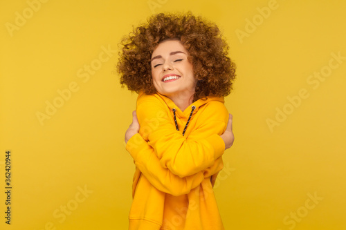 Εκτύπωση καμβά I love myself! Portrait of self-satisfied egoistic curly-haired woman in urban style hoodie embracing herself and smiling with pleasure, feeling self-pride