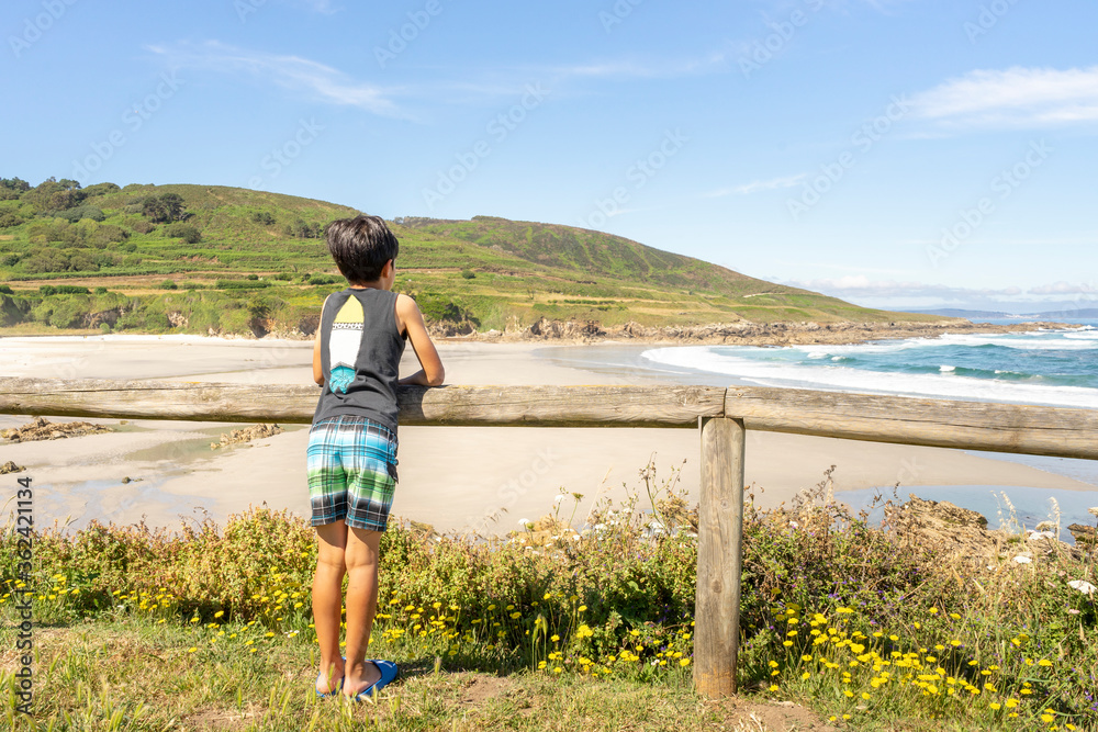 Child observing from a viewpoint a beautiful beach with a mountain in the background and a clear sky
