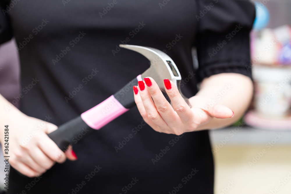 Women's hands hold a large hammer with a pink handle in a threatening or indecisive position