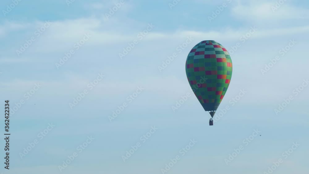 Colorful hot air balloon floating up in blue sky, birds flying trough the frame, medium distant shot Colorful hot air balloon floating up in blue sky, birds flying trough the frame, medium distant shot