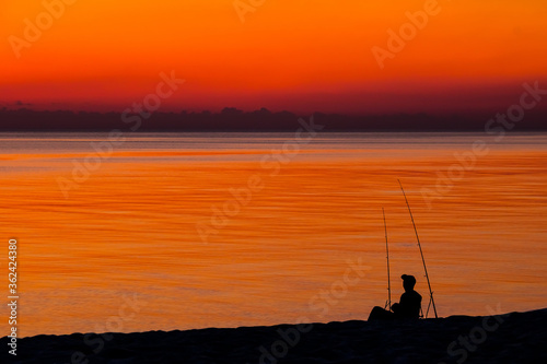 silhouettes of fishermen on the background of the orange sea