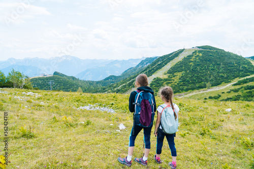 Children hiking on beautiful summer day in alps mountains Austria resting on rock. Kids look at map mountain peaks in valley. Active family vacation leisure with kids. Outdoor fun and healthy activity
