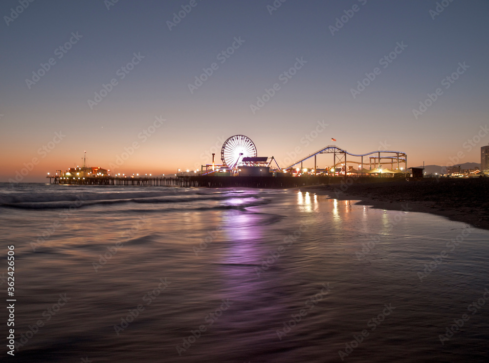 Fototapeta premium Dusk view of popular Santa Monica pier reflecting in pacific ocean water in Southern California.
