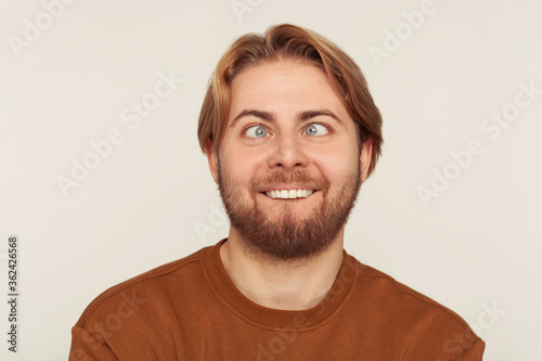 Closeup portrait of idiot, dumb bearded man looking cross-eyed with stupid smile, fooling around, making silly face, brainless comical expression. indoor studio shot isolated on gray background photo