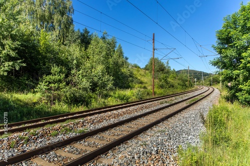 Railroad ties and track surrounded by shrubbery at a curve in Czech Republic. Close-up of a slightly rusty railway line with concrete railroad ties