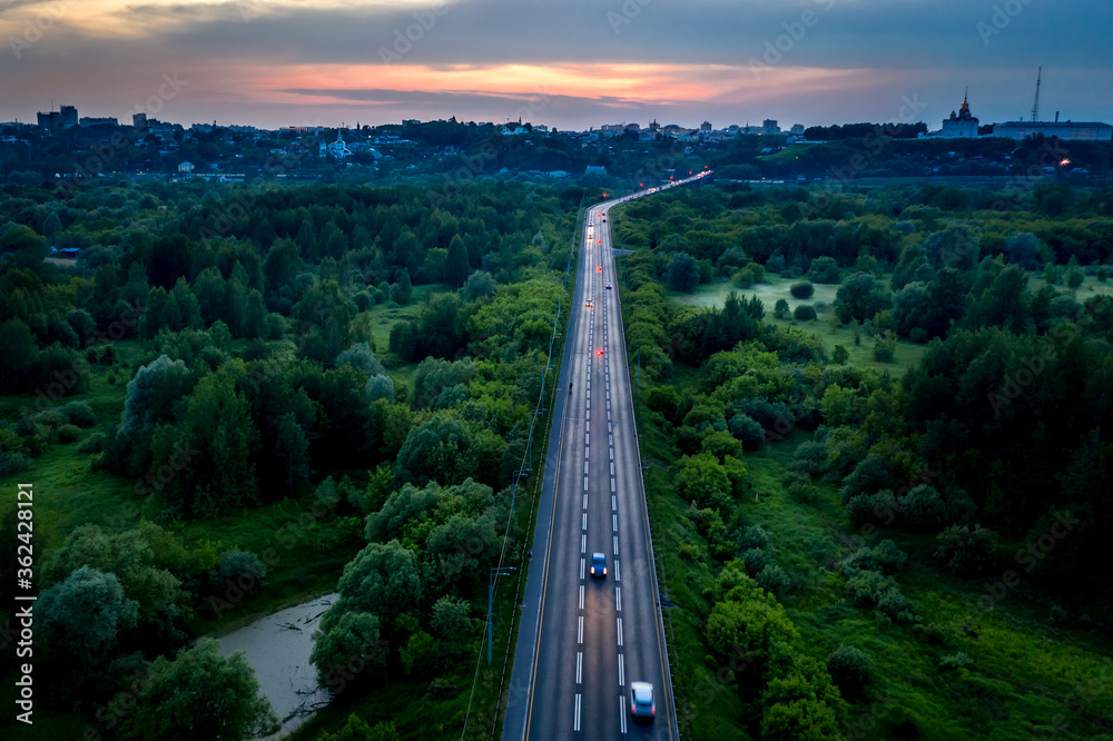 Aerial view of the asphalt road through green fields towards the city of Vladimir, Central Russia. Sunset landscape.