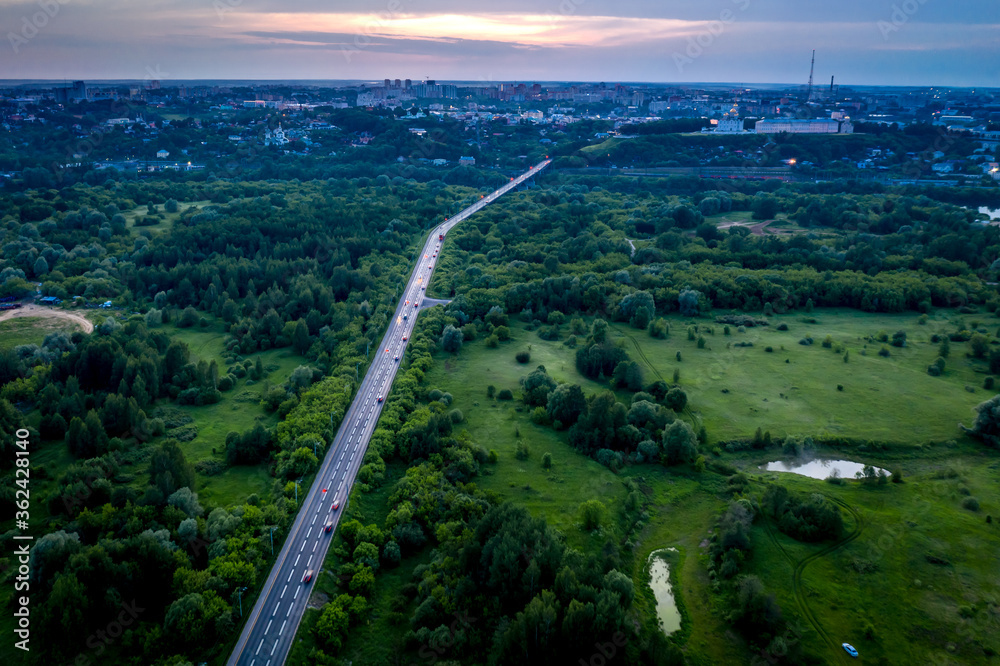Aerial view of the asphalt road through green fields towards the city of Vladimir, Central Russia. Sunset landscape.